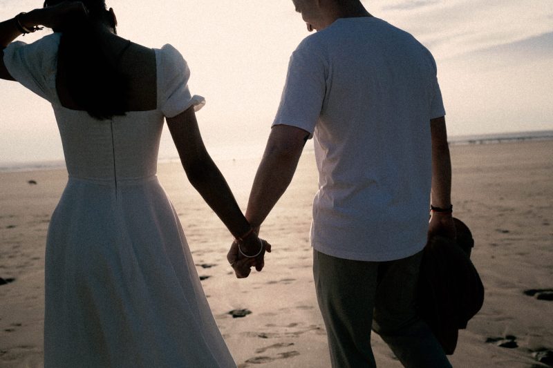 Couple holding hands on the beach at dusk.