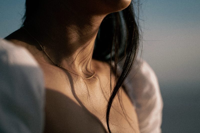 Close-up of a person's neck and shoulder area with a focus on the skin texture and a gold chain, set against a blurred background.