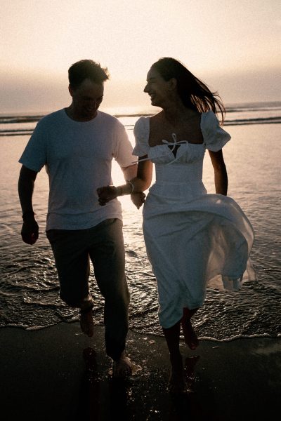 A couple holding hands and smiling at each other while walking along the beach at sunset, captured in a FREE gifbooth.