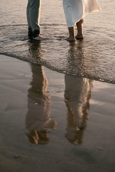 Two people walking along the shoreline, with their reflections visible on the wet sand, resembling a scene captured in a FREE gifbooth.