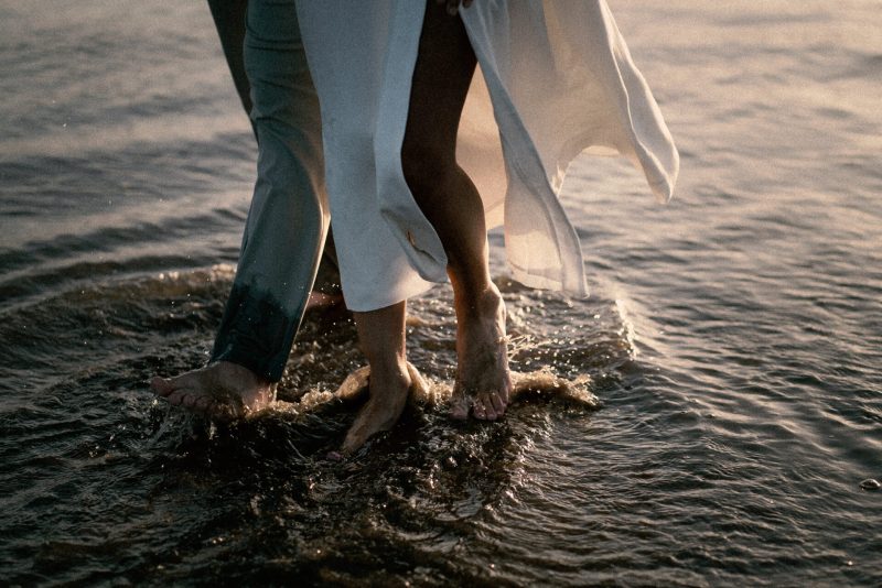 Two people wading in shallow water at sunset during a wedding.