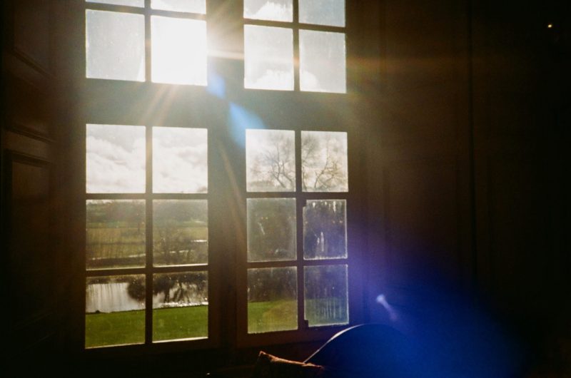 Sunlight streaming through a windowpane, casting a warm glow in a room with a view of trees and a water body outside, reminiscent of the magic mirror in its ethereal presence.