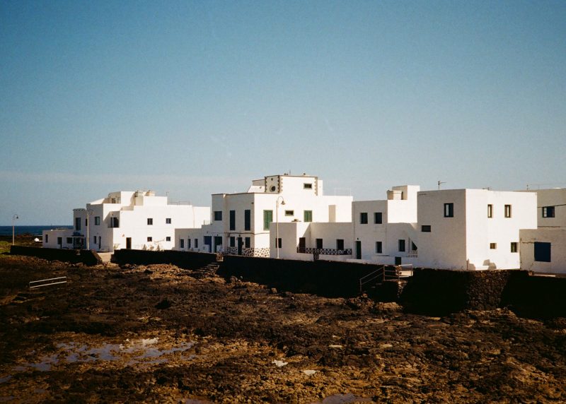 Whitewashed buildings with flat roofs on a rocky coastline under a clear blue sky, captured through the lens of a photobooth.