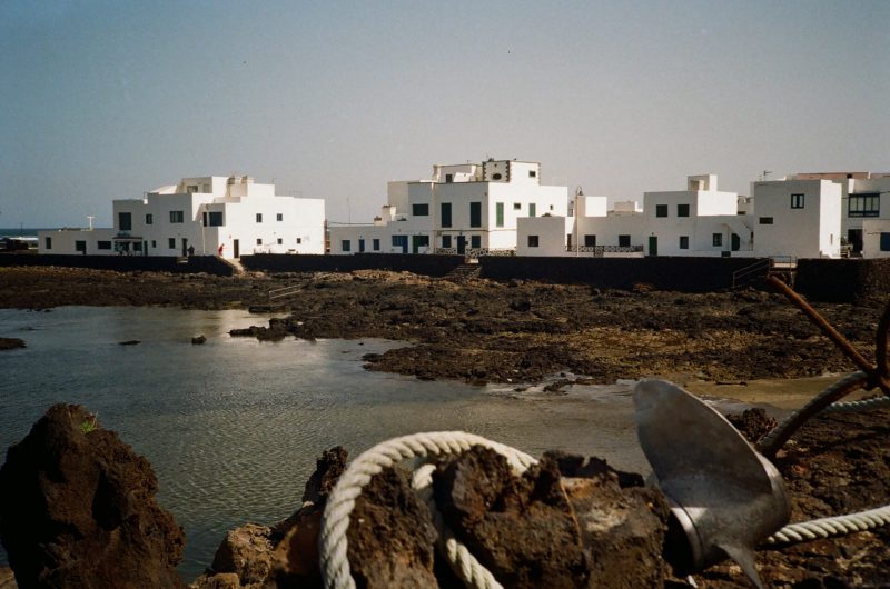 White coastal buildings beside rocky shores with a boat anchor in the foreground, perfect for a wedding gifbooth setup.