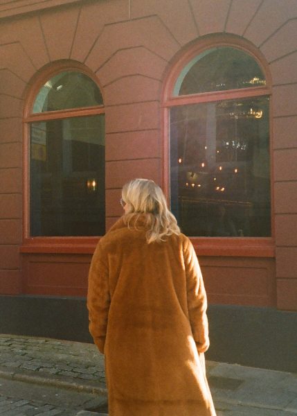 A person in a brown coat walking past a building with FREE arched windows.