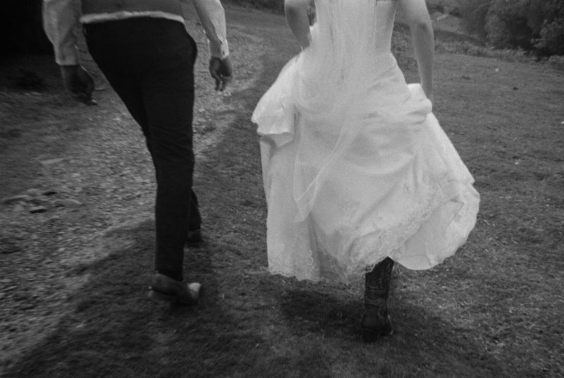 A bride and groom walking through a field, captured in a close-up of their lower halves at their wedding.