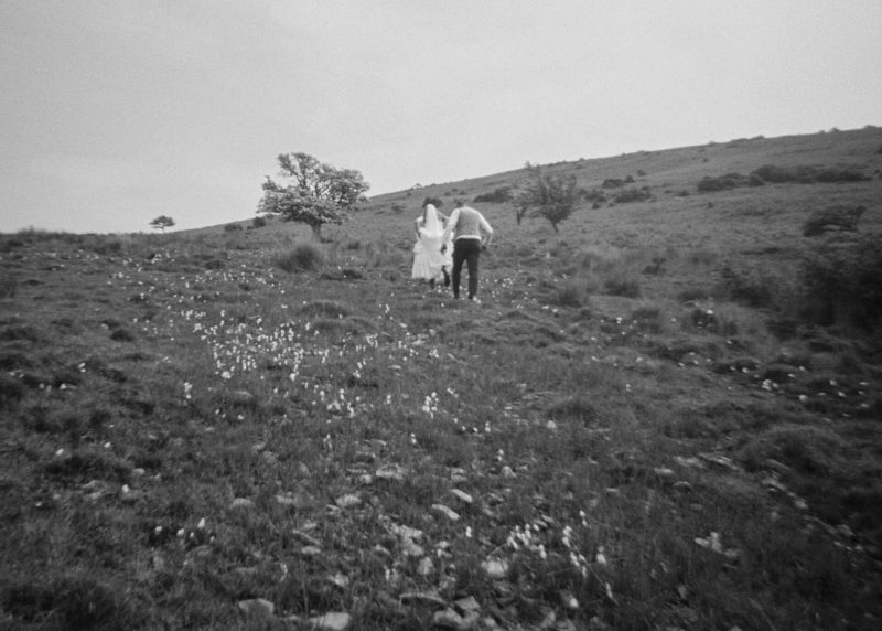 Two people walking up a grassy hillside toward a FREE photobooth at a wedding.