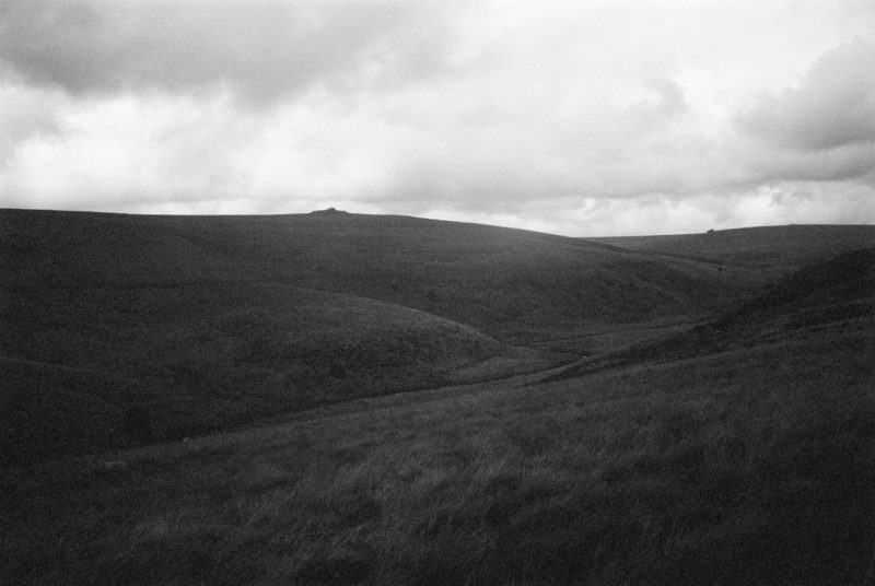 Rolling hills under a cloudy sky in a monochrome landscape, captured through the lens of a magic mirror.
