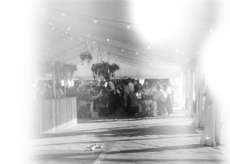 Outdoor wedding event under a tent with string lights and guests mingling.