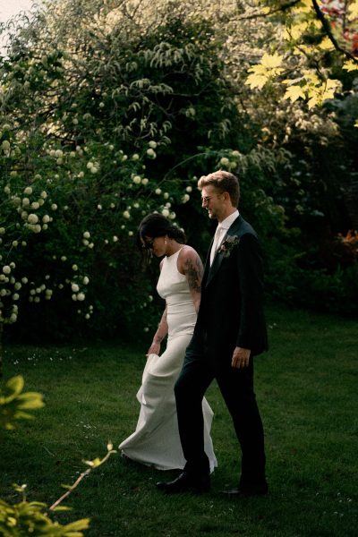 A couple dressed in wedding attire walking through a garden.