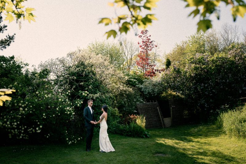 A couple in wedding attire holding hands in a lush garden.