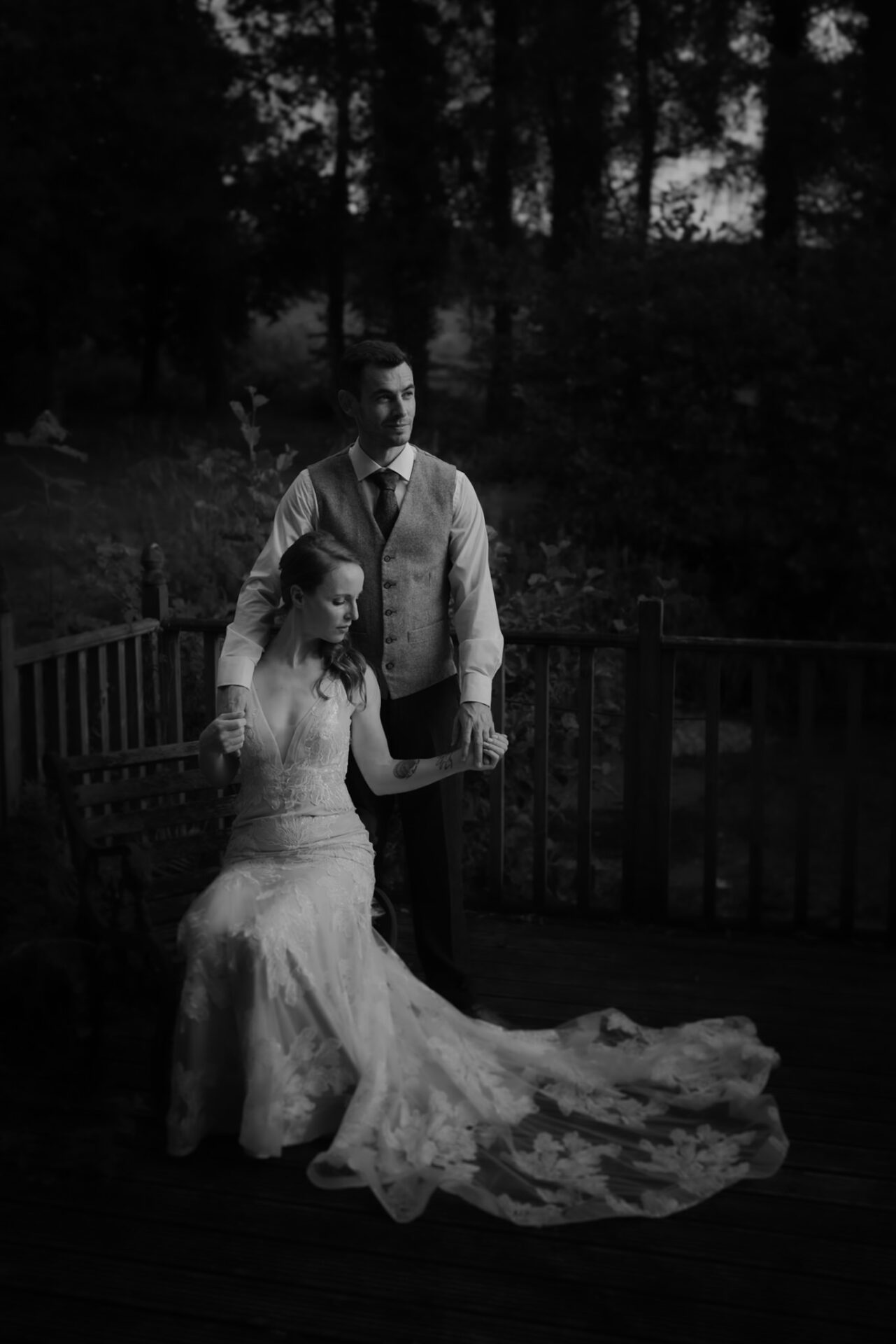 A bride and groom in elegant attire posing on a wooden deck at twilight, surrounded by soft-focused trees from our exclusive wedding photography collection.